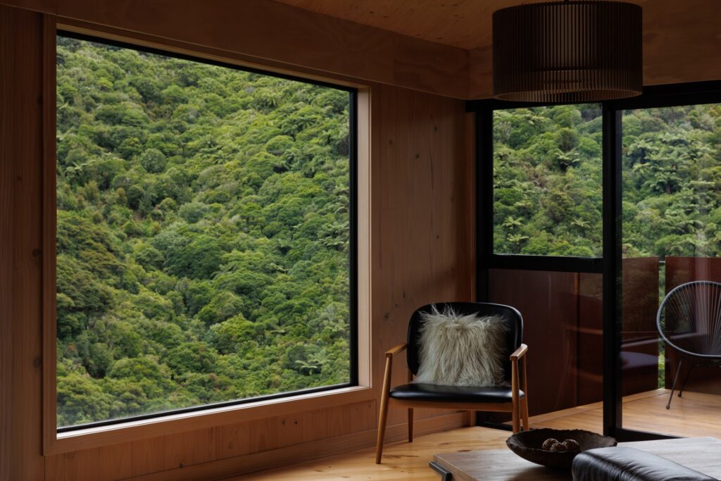 Timber-lined corner with window seat and an oversized opening framing close-range bush.
