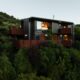 Golden Bay House nestled in steep bush at dusk, dark cladding and corten balconies lit from within.