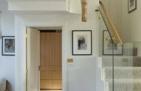 Sculptural timber pendant with red interior hanging in the stair lightwell above carpeted stairs and glass balustrade.