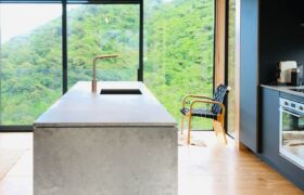 Modern coastal architecture with bush-clad hillside and Tasman region backdrop