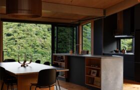 Kitchen and dining with dark cabinetry and full-height glazing opening to the bush canopy.